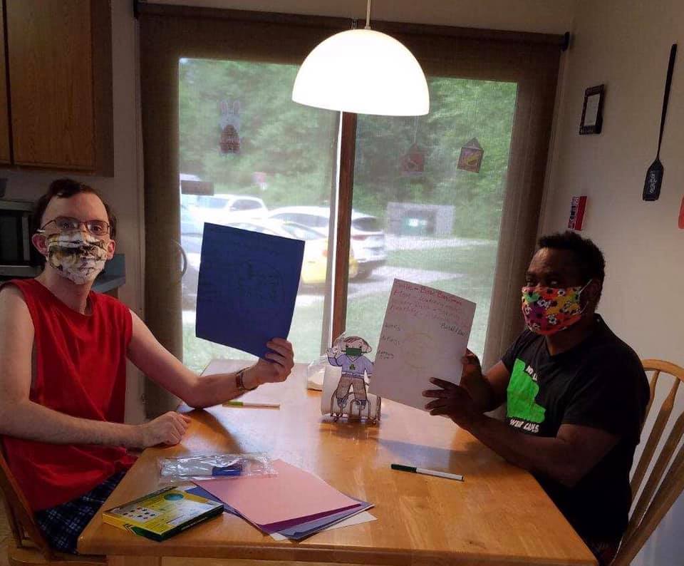 Picture of two men holding up pieces of paper, sitting at a kitchen table